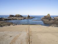 a paved sidewalk leading into the ocean and some rocky cliffs in the background of the ocean