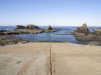 a paved sidewalk leading into the ocean and some rocky cliffs in the background of the ocean