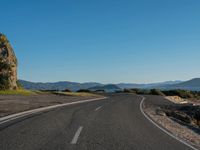 road near mountain with mountain range with lake in background and blue sky above it in daytime