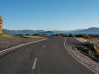 road near mountain with mountain range with lake in background and blue sky above it in daytime