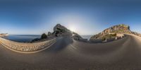 a fisheye lens image of an empty road near the ocean with mountains in the background