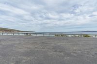 a paved parking lot with a fence and ocean in the background as seen from the side of the road