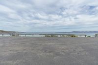 a paved parking lot with a fence and ocean in the background as seen from the side of the road