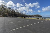 a empty parking lot sitting next to the ocean with mountains in the background and cloudy sky