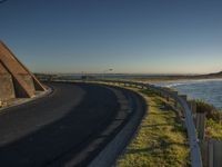 a long winding road next to the ocean at sunset time, next to an entrance for a beach