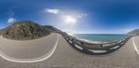 a 360 - view of the ocean on a road with a fence in front of it