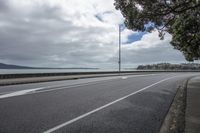 a wide, empty road going past a beach side wall with large water in the background