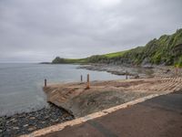 a walkway next to the ocean with a small boat parked in it on rocks and dirt