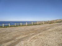 a person walking down a dirt road next to the ocean on a clear day near the beach