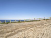 a person walking down a dirt road next to the ocean on a clear day near the beach