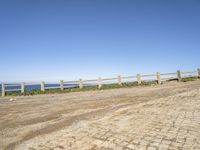 a person walking down a dirt road next to the ocean on a clear day near the beach