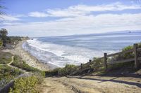 an oceanfront area next to a wooden rail railing with a bench overlooking the beach