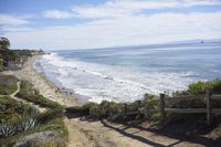 an oceanfront area next to a wooden rail railing with a bench overlooking the beach