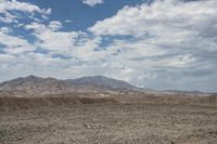 clouds hang over the mountainous terrain on an arid plain in the desert, with sparse trees around