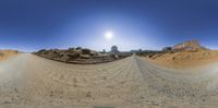 a spherical panorama with a sun shining over some hills and dirt roads and sand dunes