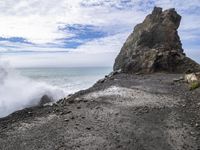 waves crashing on the shoreline with rocks and rock formations on a beach next to the water