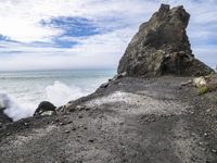 waves crashing on the shoreline with rocks and rock formations on a beach next to the water