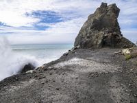 waves crashing on the shoreline with rocks and rock formations on a beach next to the water