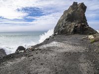 waves crashing on the shoreline with rocks and rock formations on a beach next to the water