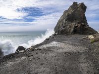 waves crashing on the shoreline with rocks and rock formations on a beach next to the water