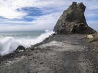 waves crashing on the shoreline with rocks and rock formations on a beach next to the water