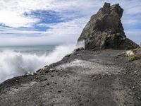 waves crashing on the shoreline with rocks and rock formations on a beach next to the water