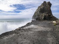 waves crashing on the shoreline with rocks and rock formations on a beach next to the water