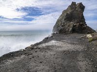 waves crashing on the shoreline with rocks and rock formations on a beach next to the water