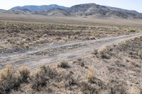 a dirt road in the middle of dry, arid terrain and mountains in the distance