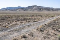 a dirt road in the middle of dry, arid terrain and mountains in the distance