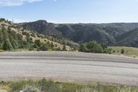 a small empty dirt field and a forest behind it on a sunny day with hills and mountains in the background