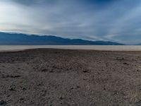 a barren area with dry, black and white ground and some mountains in the distance