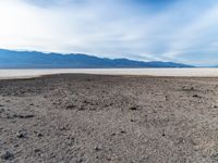 a barren area with dry, black and white ground and some mountains in the distance