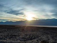 a lone motorcycle is parked by a lake with mountains in the back ground and clouds in the background