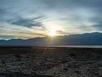 a lone motorcycle is parked by a lake with mountains in the back ground and clouds in the background