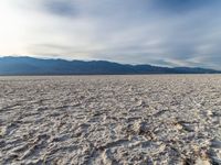 a large dry flat plain with sparse clouds in the sky and mountains behind it in the distance