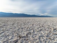 a large dry flat plain with sparse clouds in the sky and mountains behind it in the distance