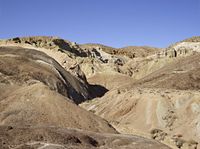 a person riding a bicycle across a dirt hillside on a sunny day and a blue sky behind