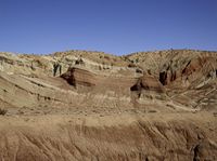 a person riding a bicycle across a dirt hillside on a sunny day and a blue sky behind