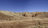 a person riding a bicycle across a dirt hillside on a sunny day and a blue sky behind