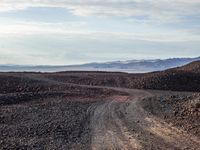 gravel road leading to distant mountains with clouds in the sky on a cloudy day,