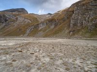 mountains with many rock formations in the foreground and a sparse grassy field with small grass