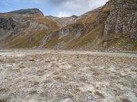 mountains with many rock formations in the foreground and a sparse grassy field with small grass