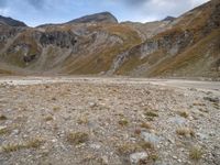 mountains with many rock formations in the foreground and a sparse grassy field with small grass