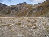 mountains with many rock formations in the foreground and a sparse grassy field with small grass