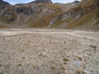 mountains with many rock formations in the foreground and a sparse grassy field with small grass