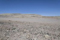 a dirt road is surrounded by some hills and desert like terrain as the vehicle sits on it