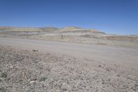 a dirt road is surrounded by some hills and desert like terrain as the vehicle sits on it