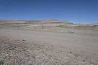 a dirt road is surrounded by some hills and desert like terrain as the vehicle sits on it