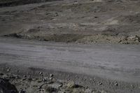 a dirt road in a barren landscape with gravel, rocks and dirt ground and a few rocks on either side